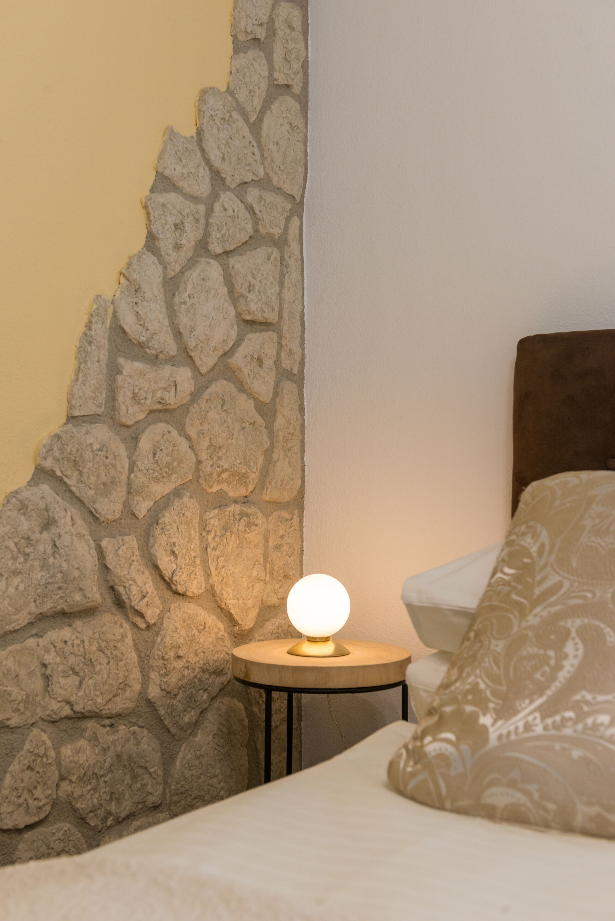 A bed with a headboard, a bedside lamp, and a stone wall.