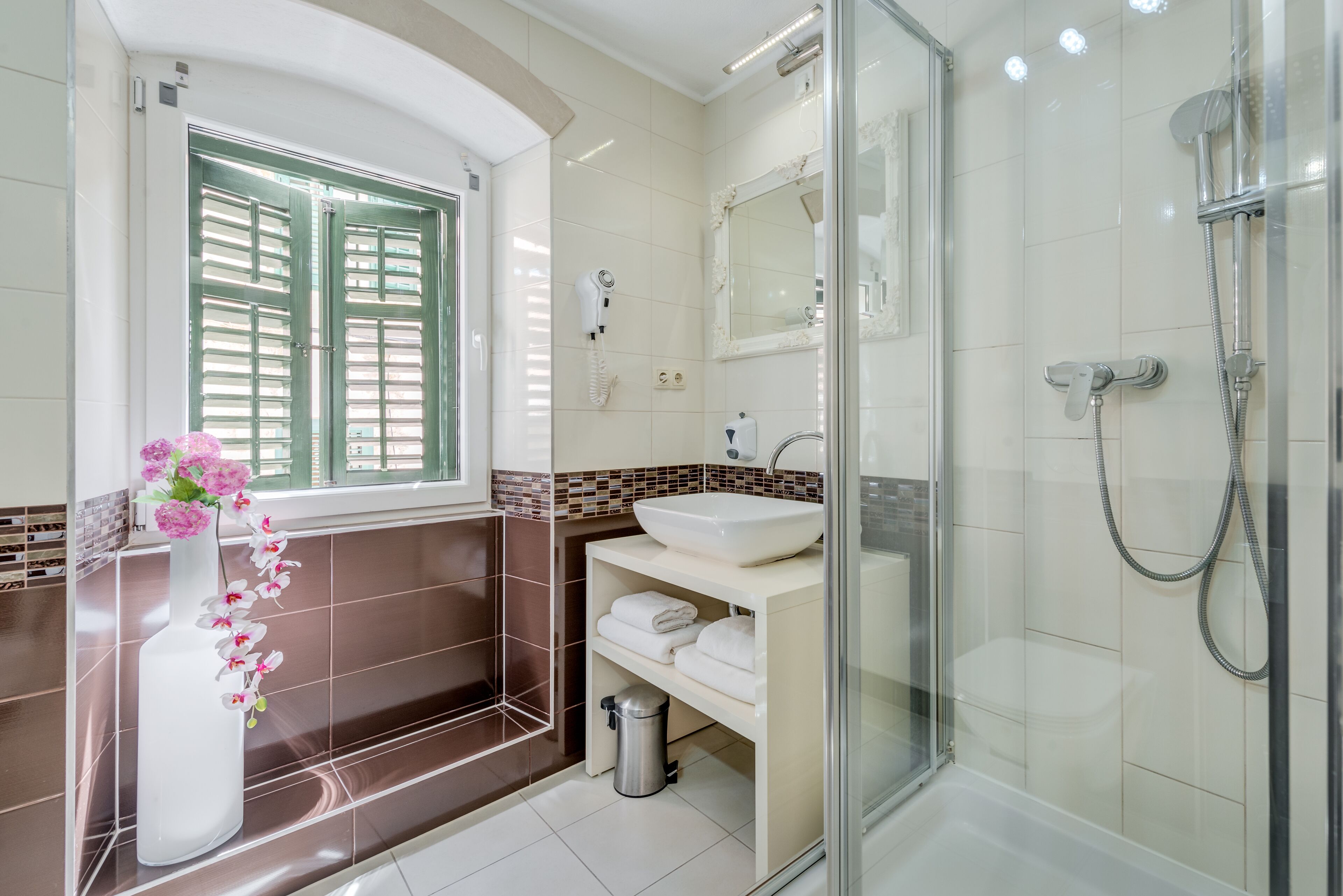 A modern bathroom with a glass-enclosed shower, a white sink, and a vase with pink flowers.