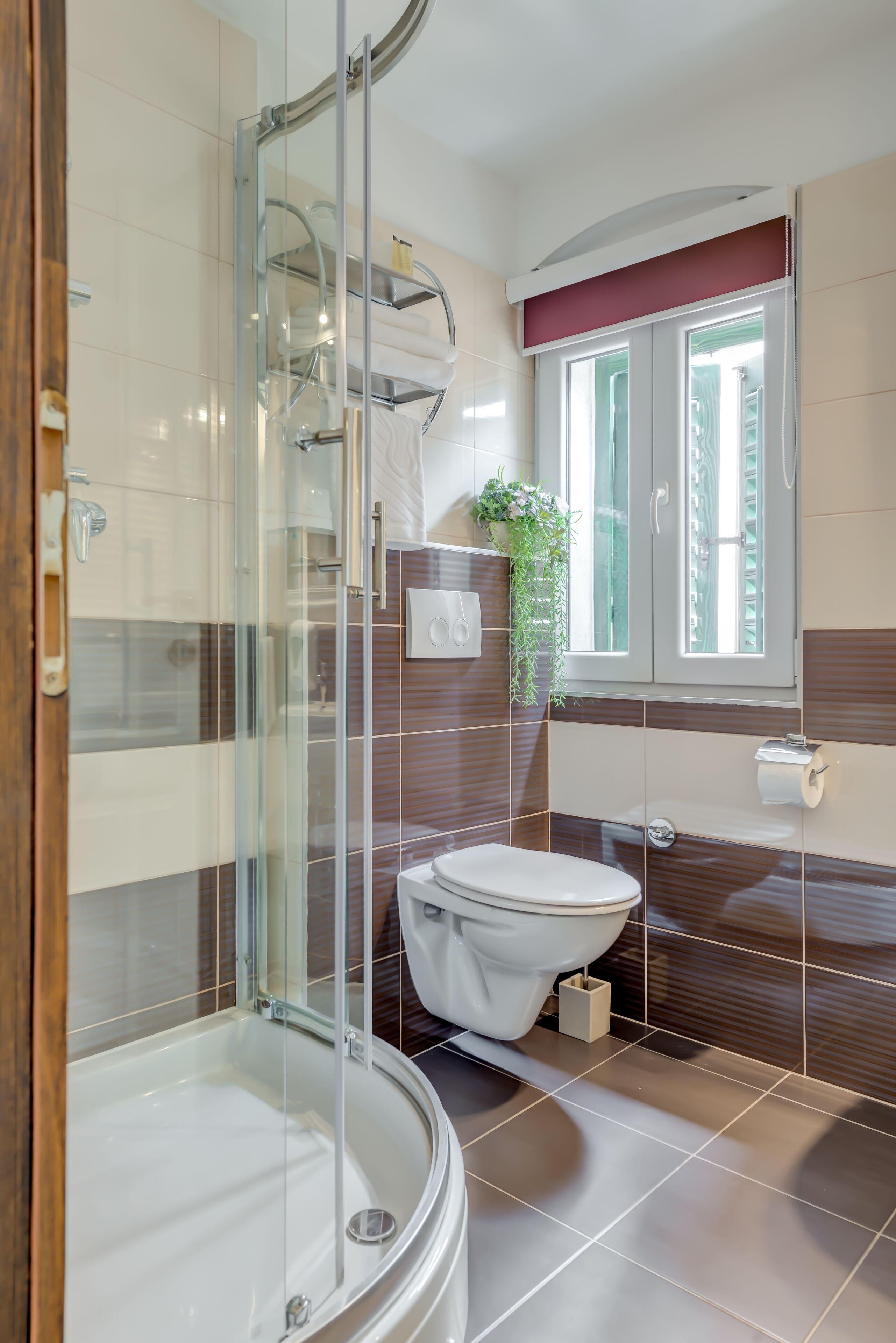 A modern bathroom with a glass-enclosed shower, a white toilet, and a window with a view of greenery.