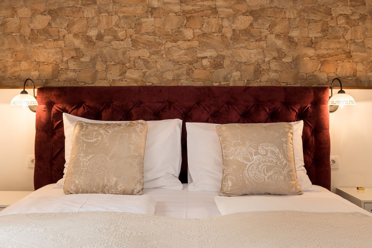 A bed with a stone wall headboard, two bedside lamps, and a white bedspread.