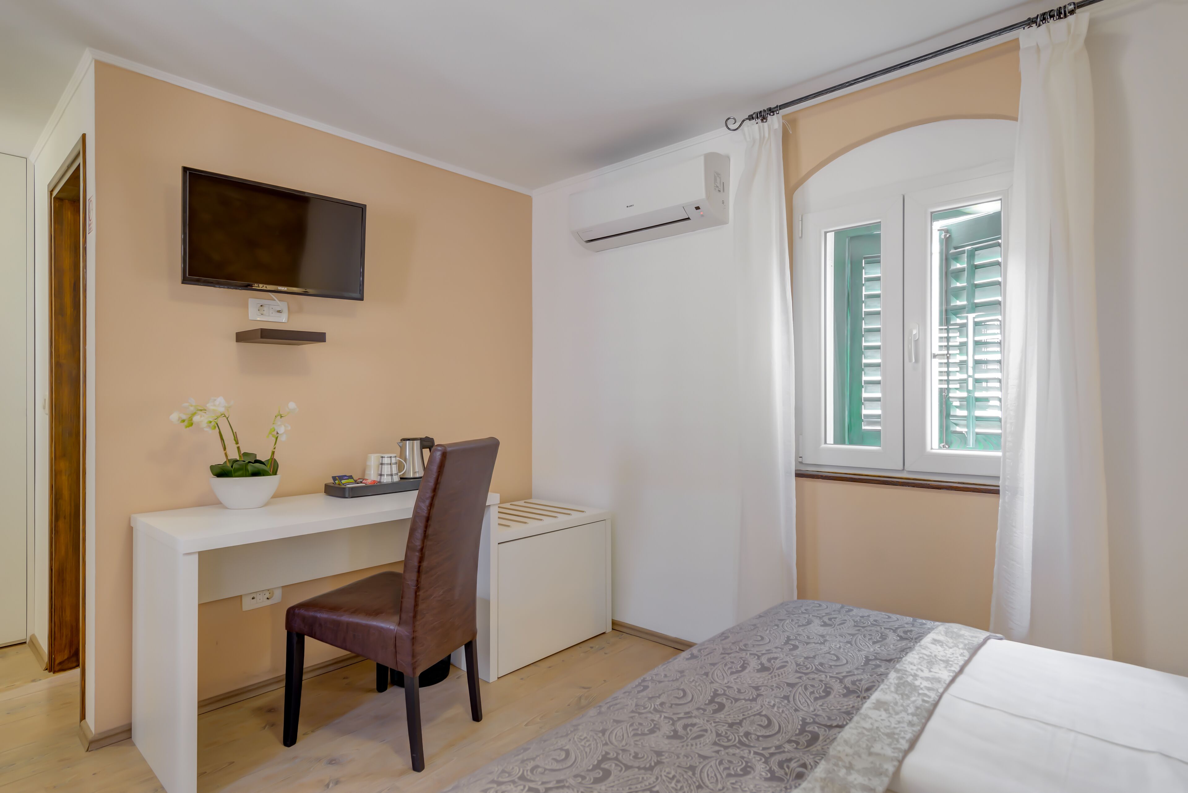 Una camera da letto con un letto, una scrivania con una sedia, una TV, un condizionatore d'aria e una finestra con persiane.