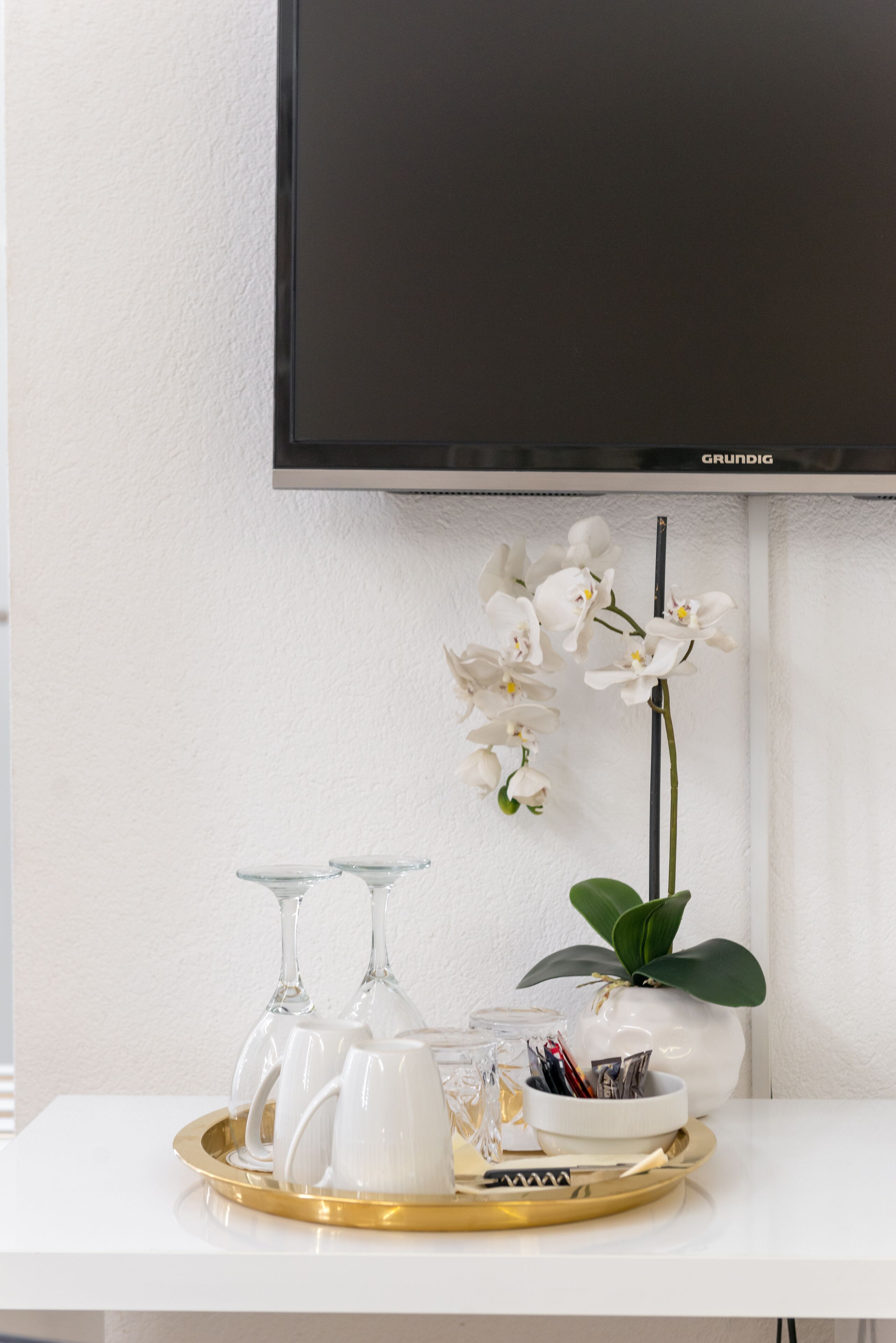 A white table with a tray holding white cups and a vase with white orchids.