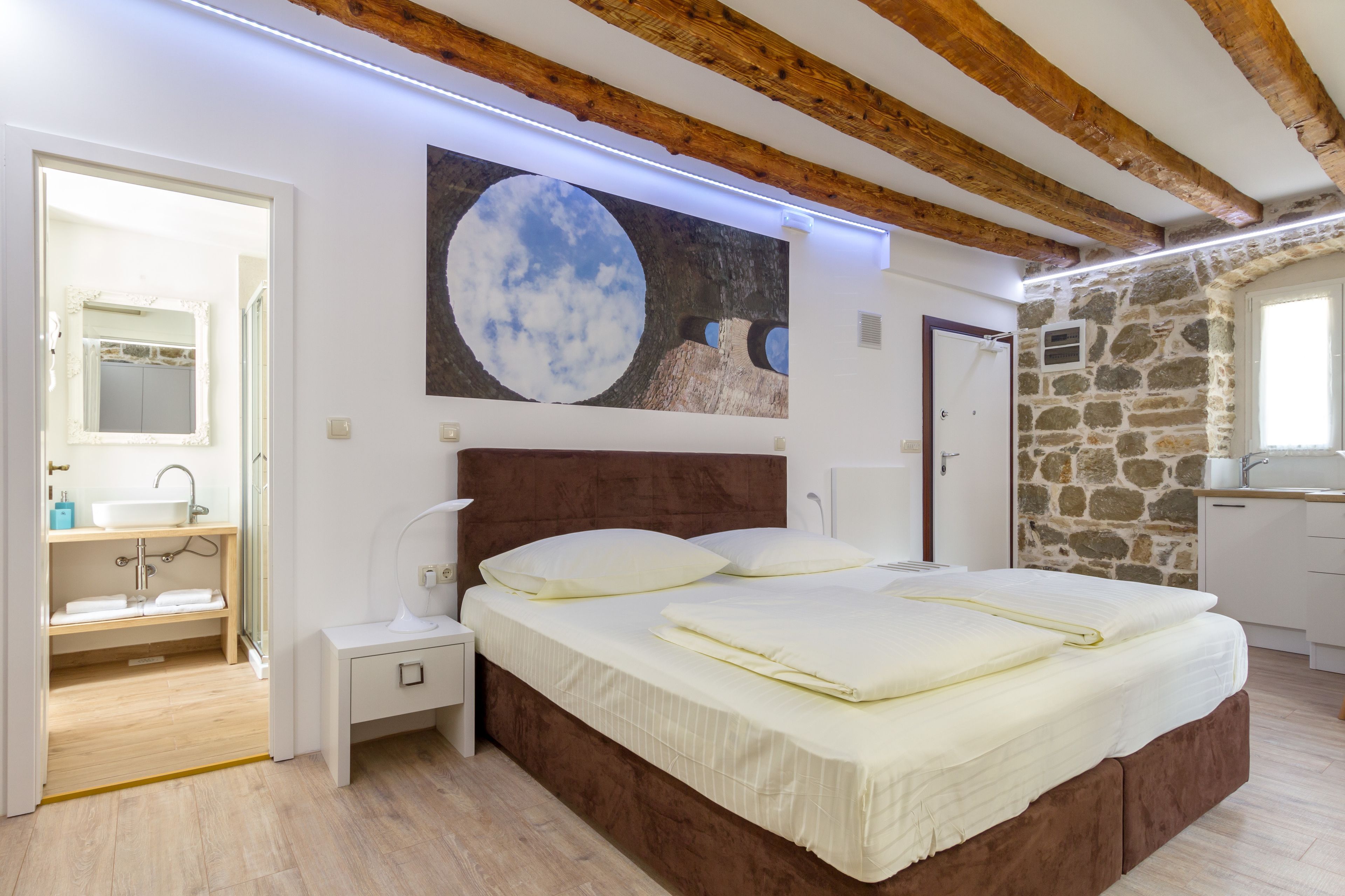 A bedroom with a large bed, a nightstand, a mirror, and a stone wall.
