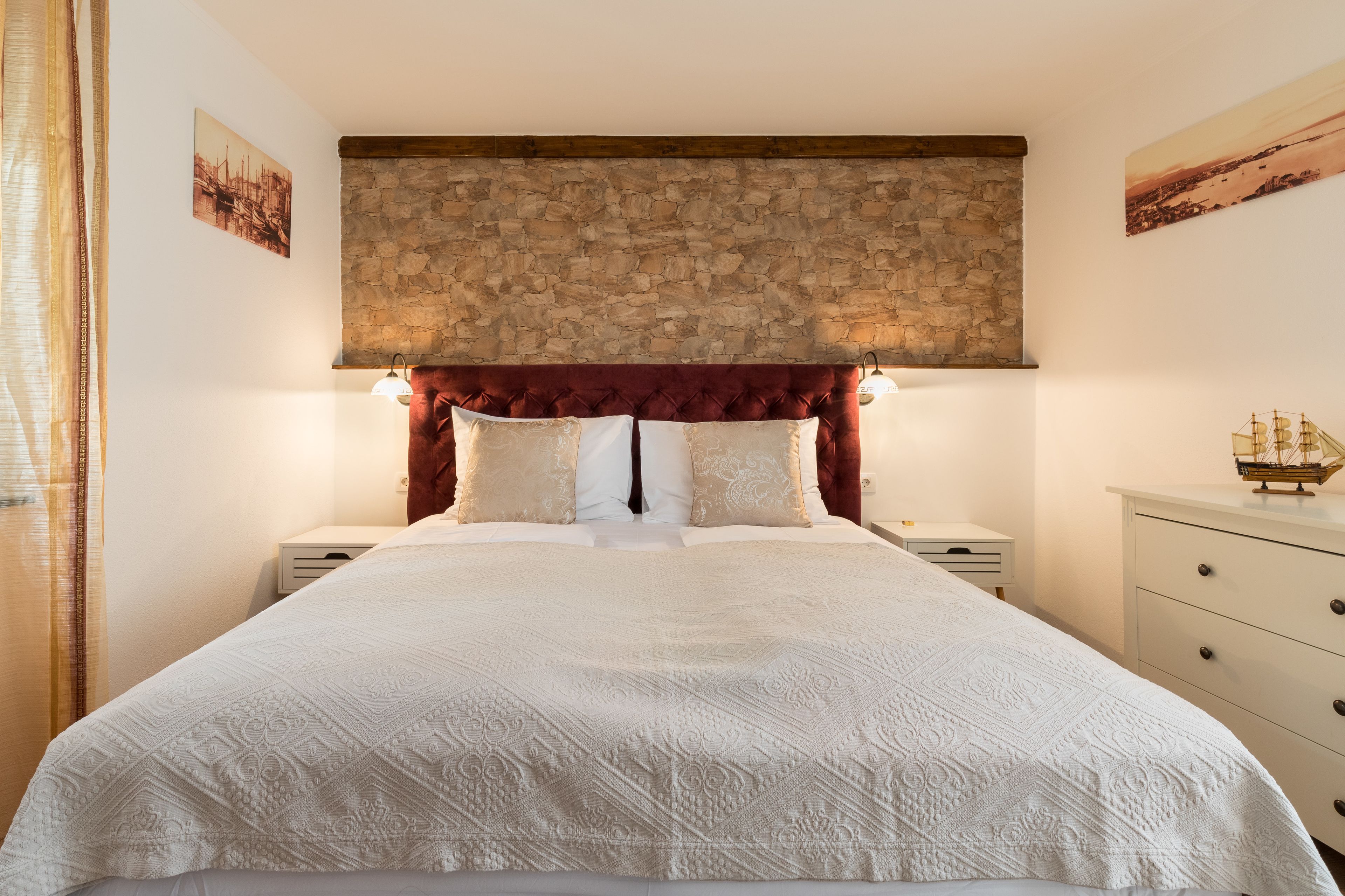 Een slaapkamer met een stenen hoofdbord, een groot bed met witte lakens, twee nachtkastjes en een bijzettafeltje.