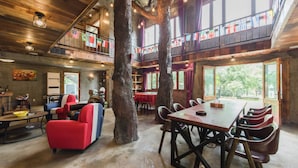 A rustic interior with a dining area, red and blue chairs, a large tree, and a balcony with flags. - Moganshan Jianqi Inn (Huzhou)