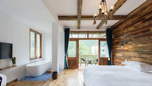 A bedroom with a large bed, a bathtub, and a balcony with a view of greenery. - Moganshan Jianqi Inn (Huzhou)