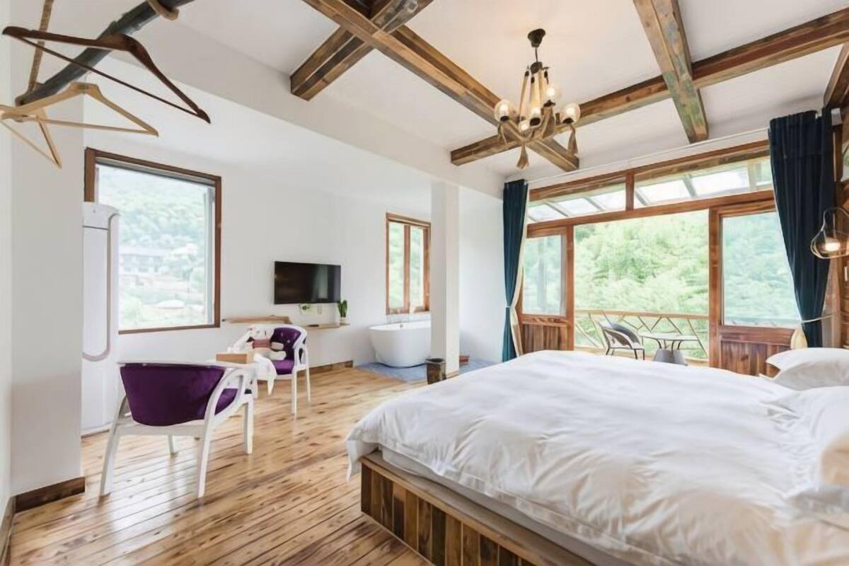 A bedroom with a large bed, a desk with a chair, a television, and a bathtub.