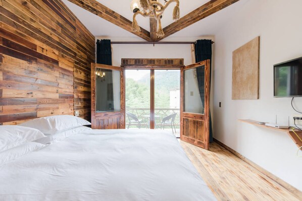 Un dormitorio con techo y paredes de madera, una cama grande, un televisor y un balcón con mobiliario exterior.
