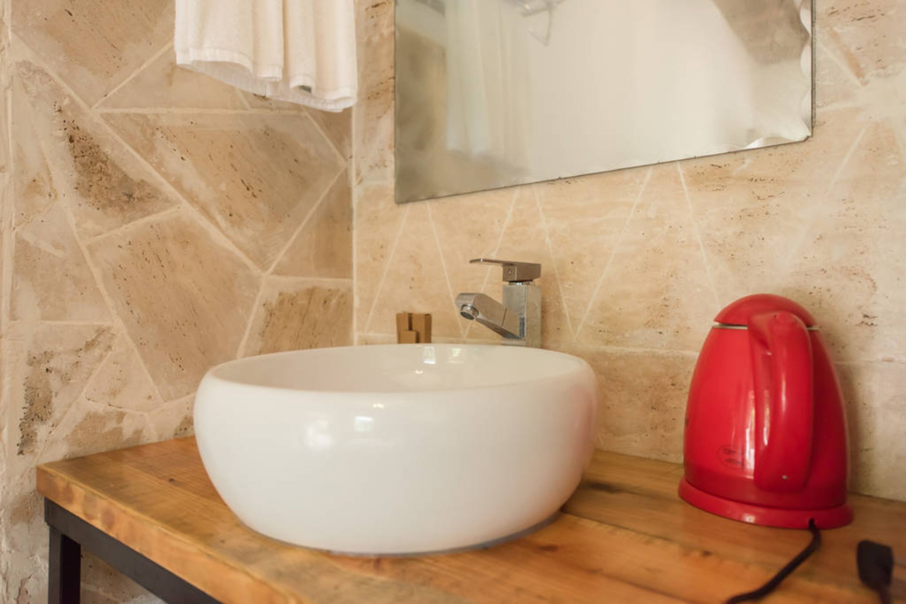 A bathroom with a white sink, a red kettle, and a mirror on the wall.