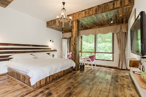 Quarto com cabeceira de madeira, uma cama grande, televisão e janela com cortinas.