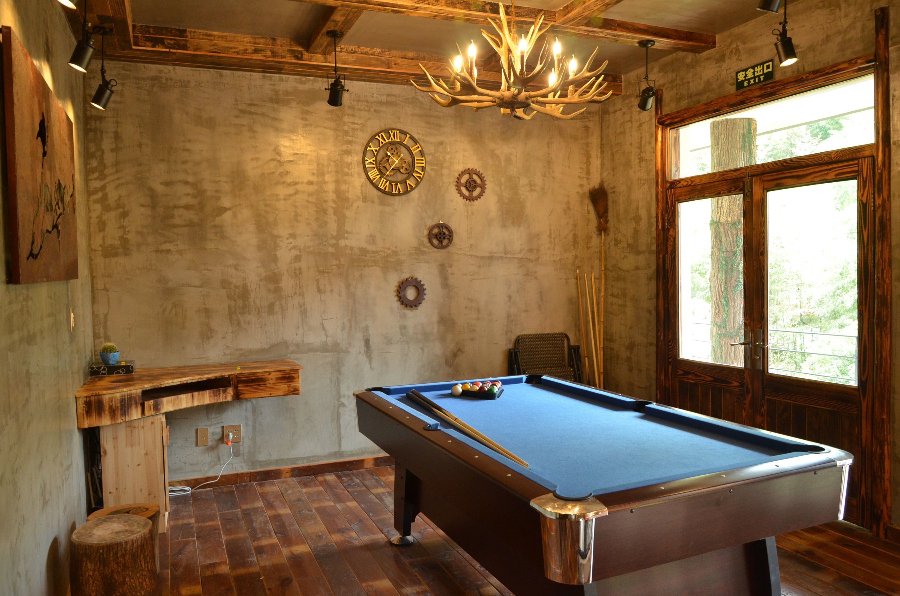 A pool table in a room with wooden floors, a chandelier, and a clock on the wall.