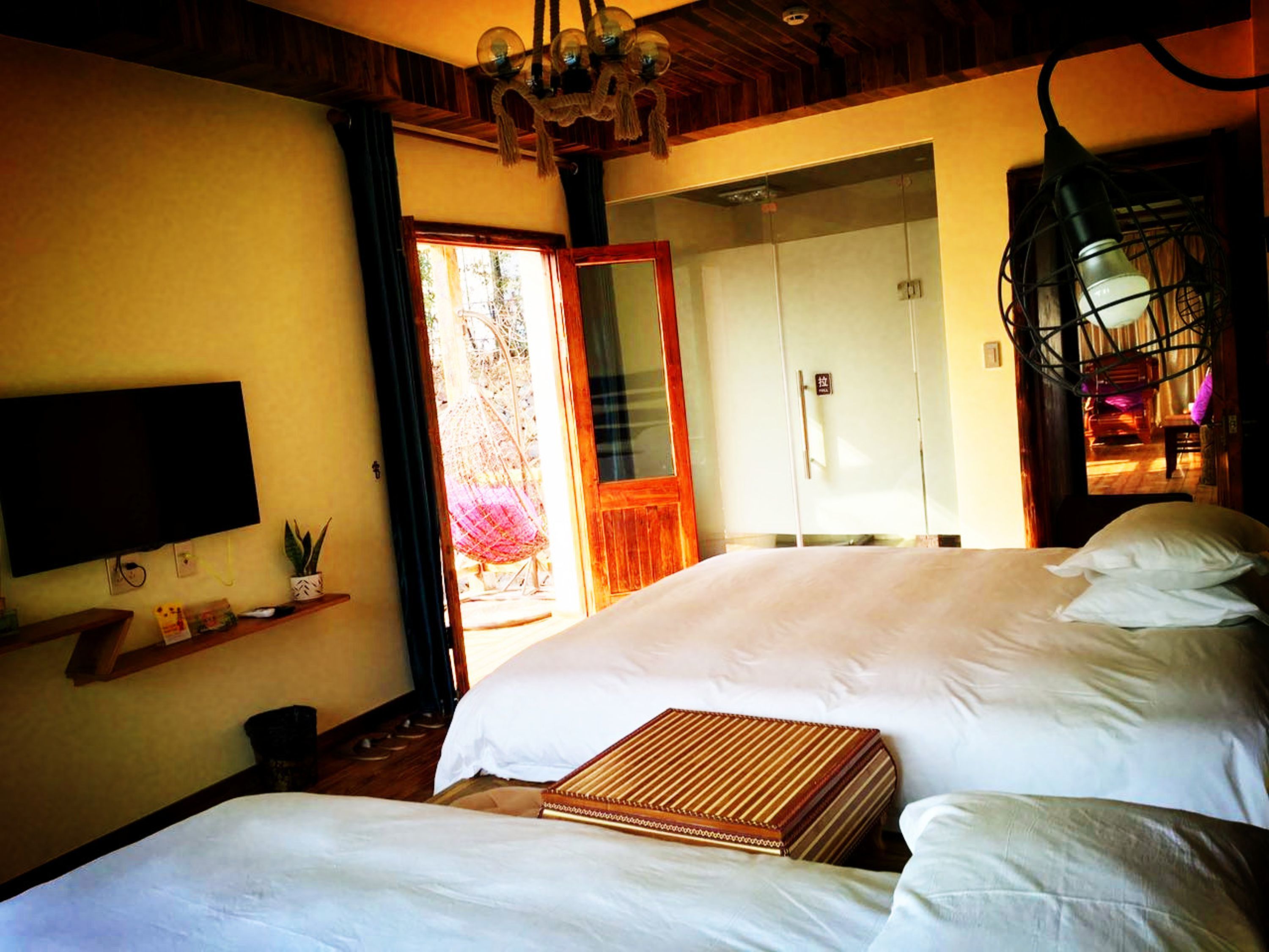 A bedroom with two beds, a TV, a shelf with items, and a door leading to a bathroom.