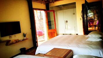 A bedroom with two beds, a TV, a shelf with items, and a door leading to a bathroom.