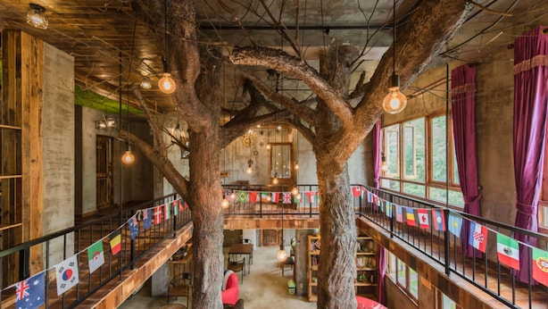 A multi-level interior with exposed wooden beams, a central tree structure, and a balcony with flags. - Moganshan Jianqi Inn (Huzhou)