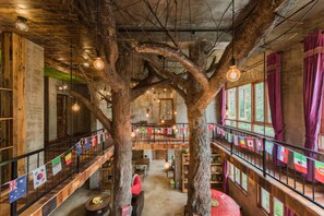 Un interior de varios niveles con vigas de madera a la vista, una estructura arbórea central y un balcón con banderas.