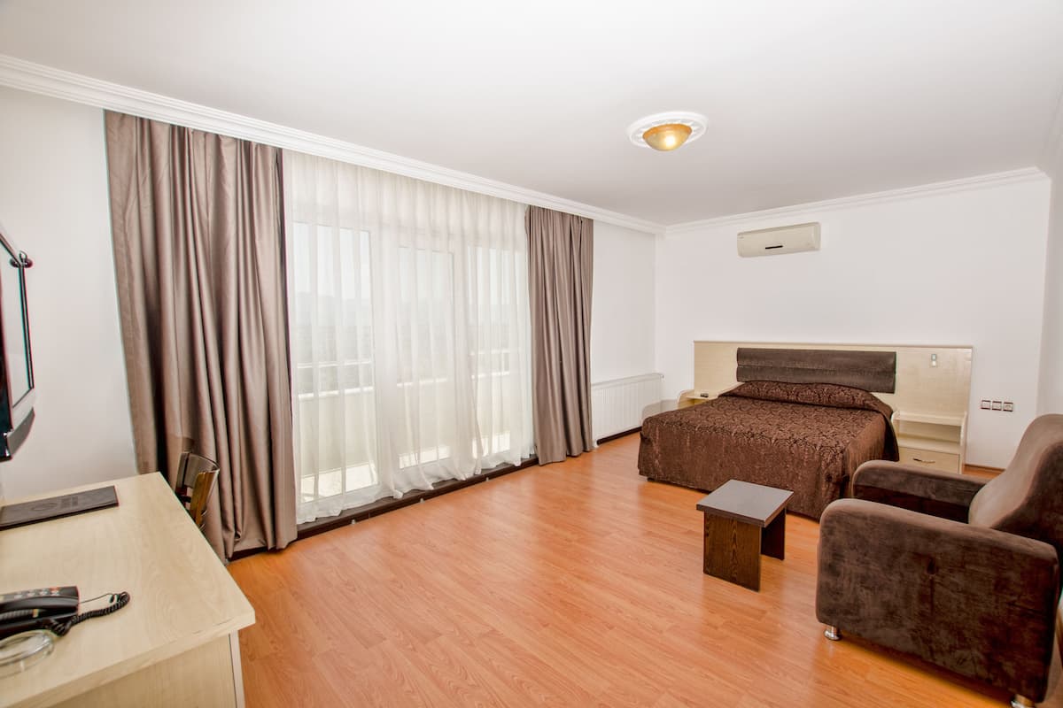 Une chambre d’hôtel avec un plancher en bois, un lit avec une tête de lit marron, un bureau avec une chaise et une petite table.