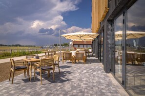 Une terrasse extérieure avec des tables et des chaises en bois, des parasols et une vue sur le ciel et le paysage.
