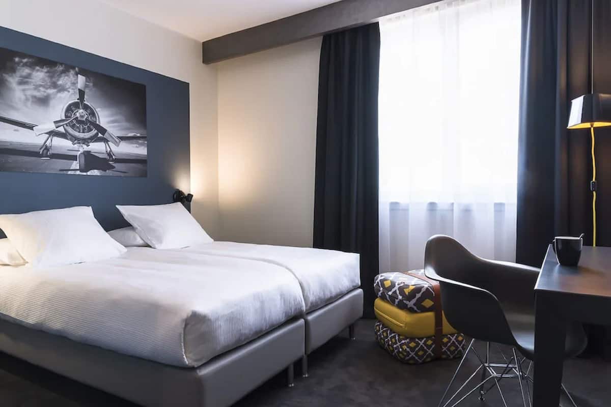 Une chambre d’hôtel avec un lit, un bureau, une chaise et une fenêtre avec des rideaux.