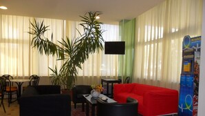 A modern living room with a red sofa, black armchairs, a coffee table with a vase, and a large potted plant.