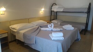 A hotel room with two single beds, a bunk bed, and a nightstand with a lamp.