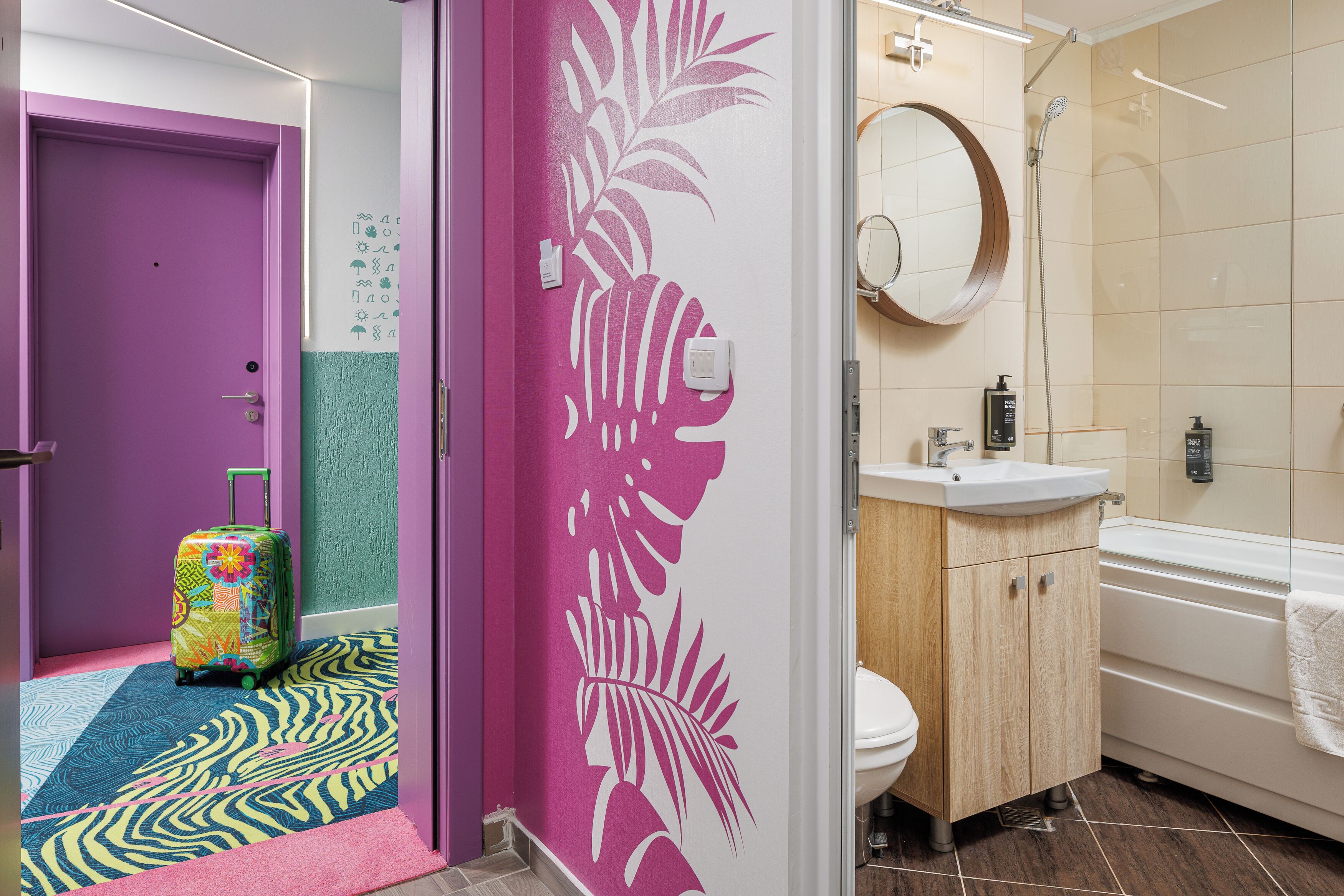 Badeværelse med bruser, toilet, håndvask og en kuffert på en måtte med zebraprint.