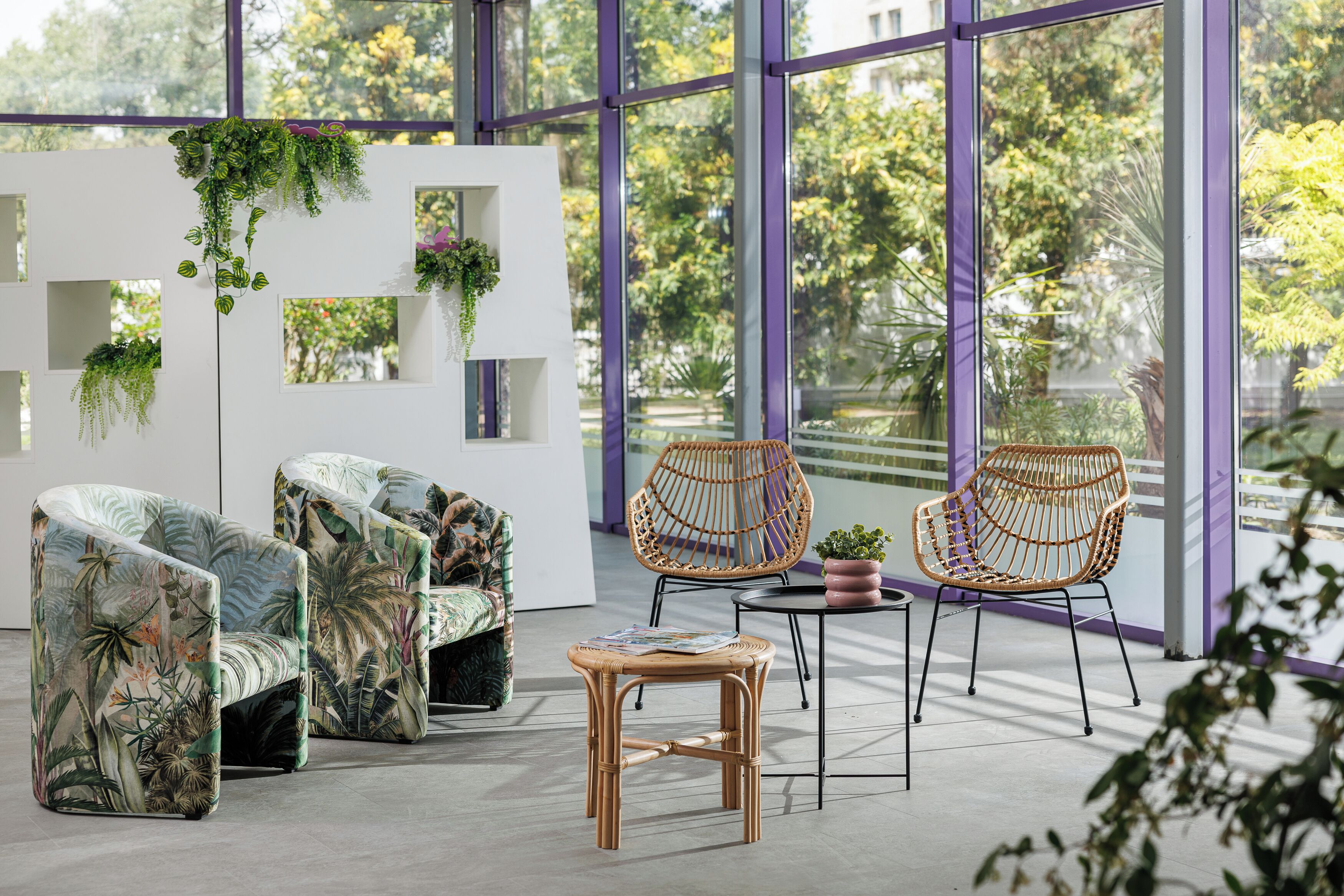 A modern interior with a white partition, two wicker chairs, a small table, and a sofa with a tropical print.