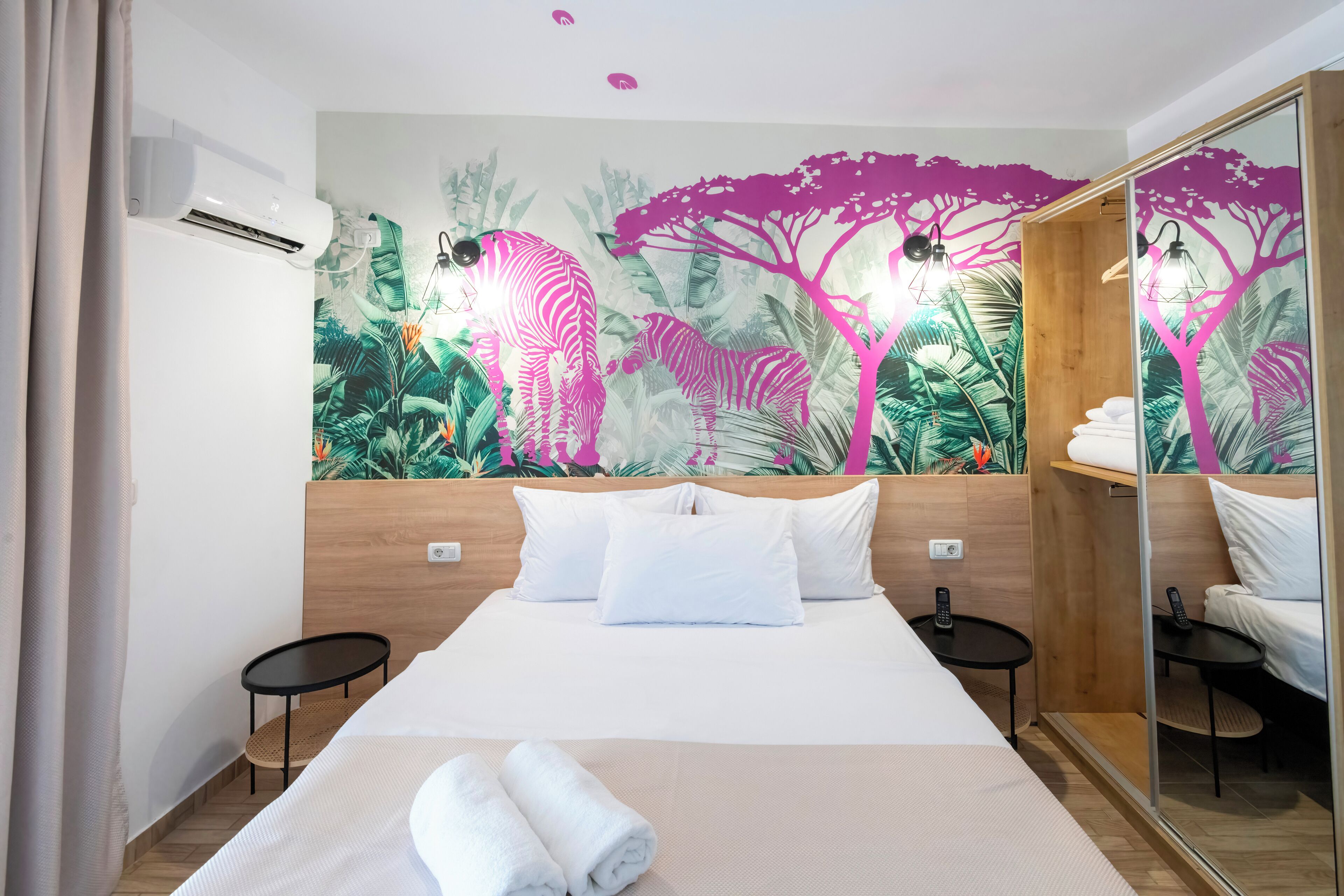 Hotelkamer met een bed, twee nachtkastjes, een muurschildering, een airconditioner en een spiegel.