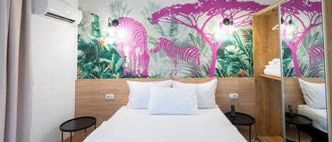 Hotelkamer met een bed, twee nachtkastjes, een muurschildering, een airconditioner en een spiegel.