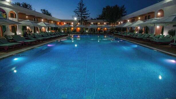 Una amplia piscina interior con sillones de descanso y sombrillas, rodeada por un edificio con varios balcones y un árbol central.