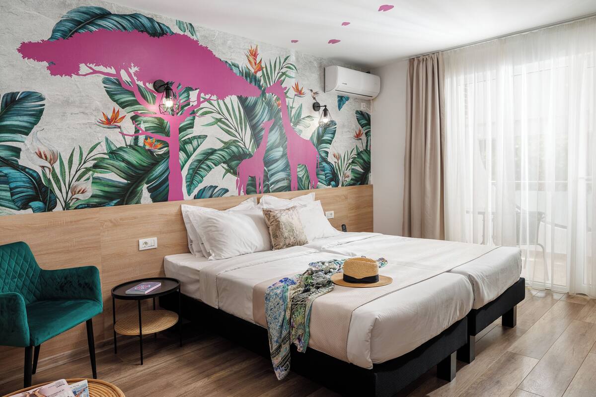 A bedroom with a bed, a chair, a small table, and a wall mural.
