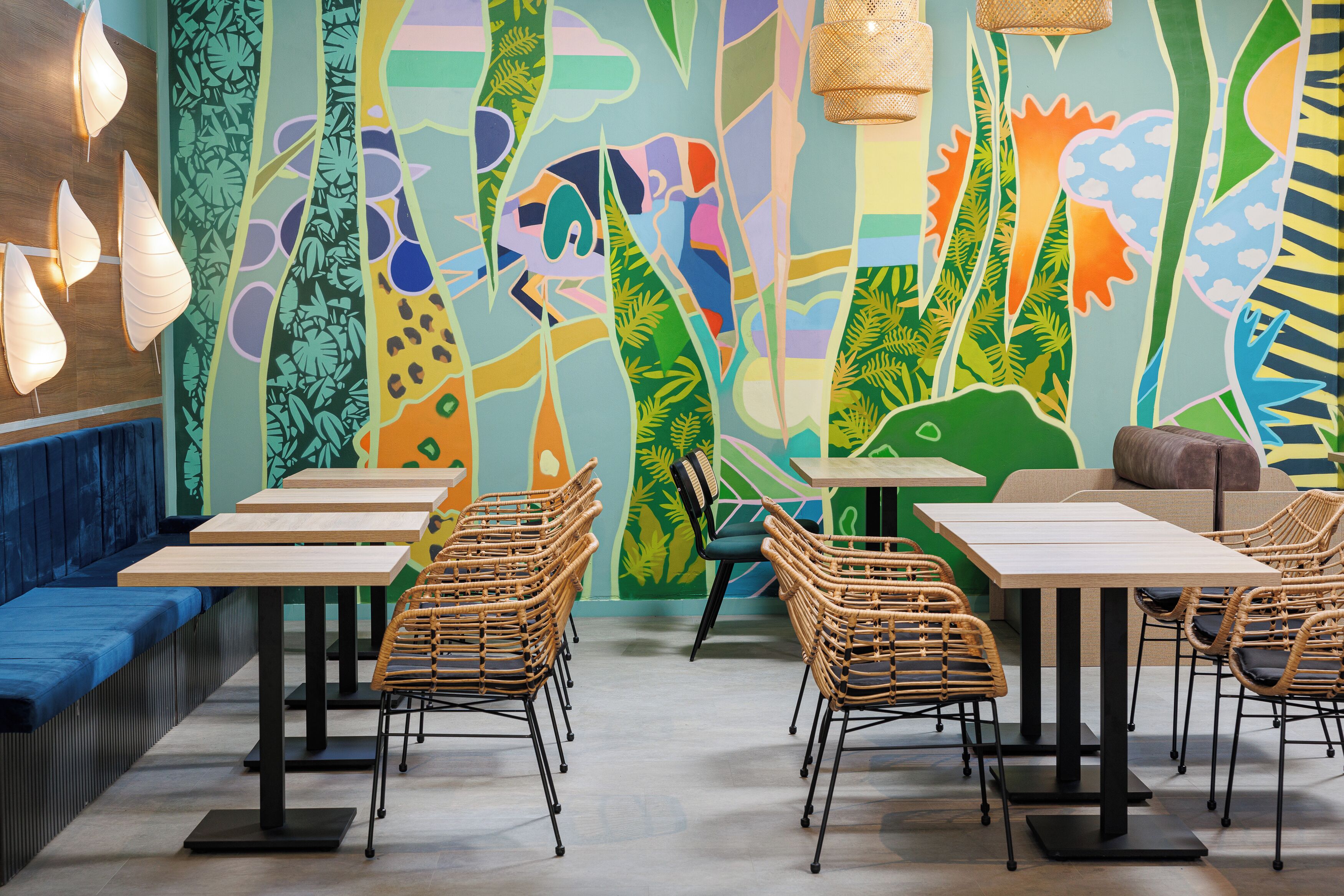 A restaurant interior with high tables, wicker chairs, and a colorful mural on the wall.