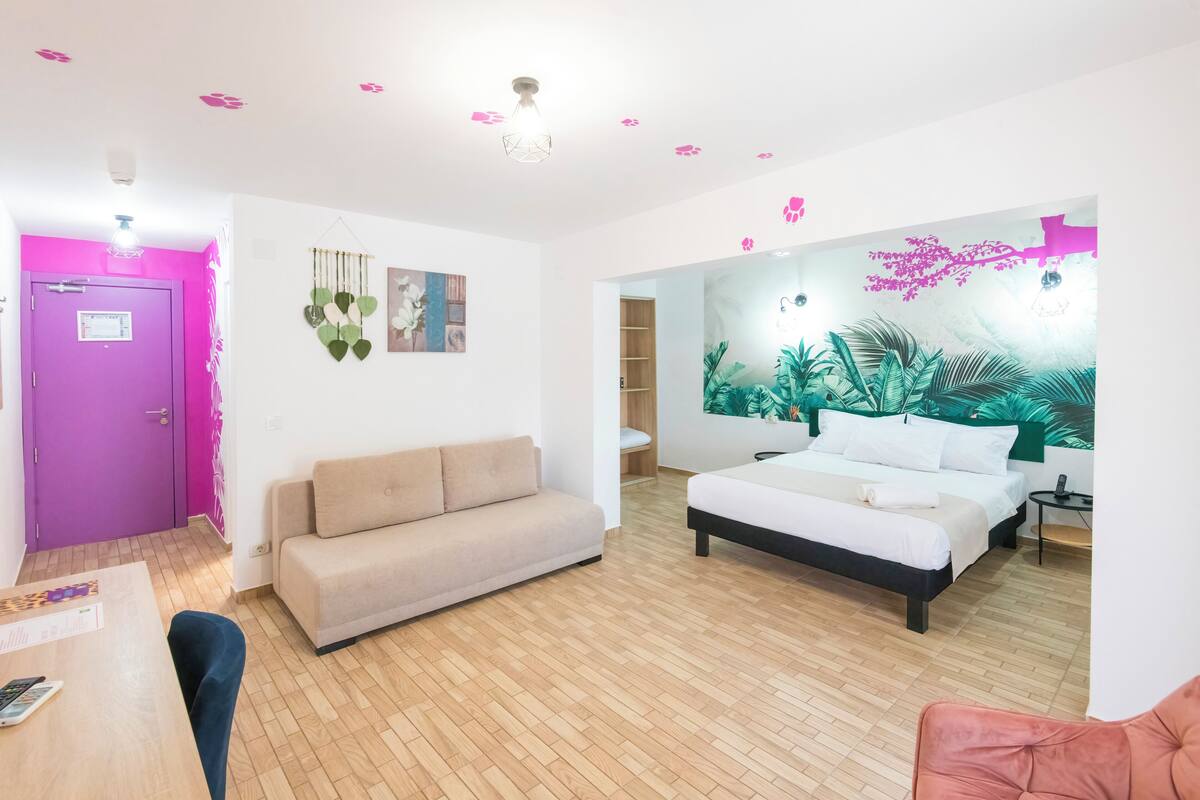 A modern hotel room with a wooden floor, a bed, a sofa, and a desk.