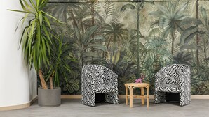 Una habitación con un gran mural de follaje tropical, dos sillas a rayas de cebra, una pequeña mesa de madera y una planta en maceta.