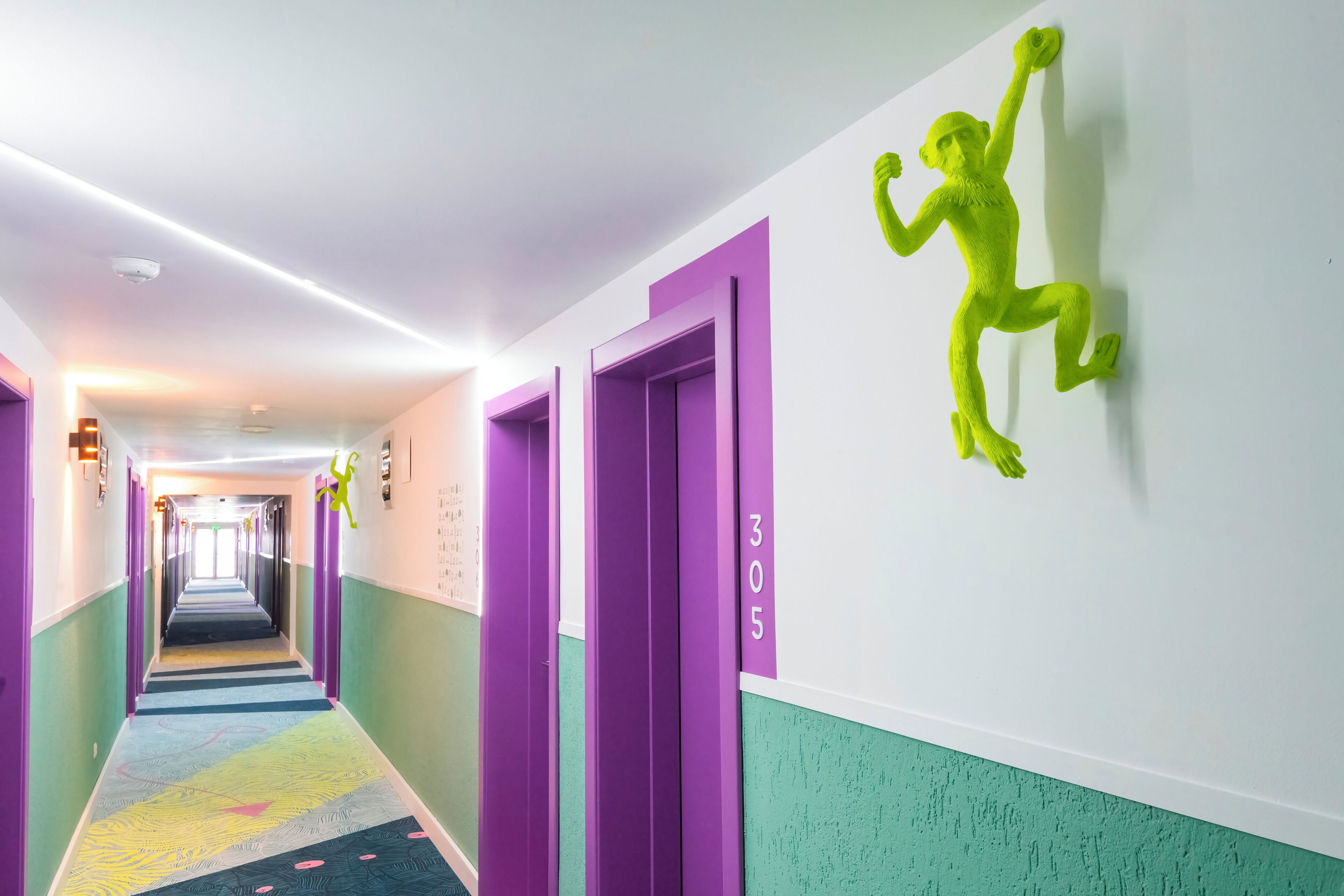 A brightly lit hallway with purple doors and a green wall sculpture.