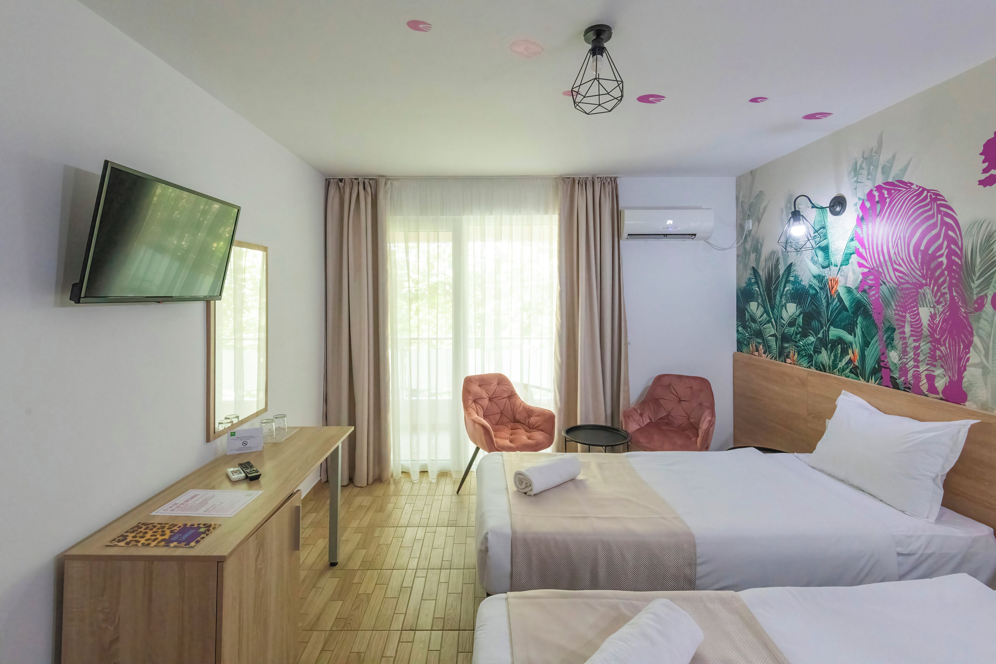 A hotel room with a bed, a desk with a chair, a television, and a wall-mounted air conditioner.