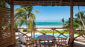 A wooden deck with a table and chairs overlooking a beach and a pool. - Zanziblue (Matemwe)