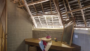 Relax in this cozy bathroom with a vaulted ceiling, wooden beams, and a natural light-filled space featuring a round basin and mirror.