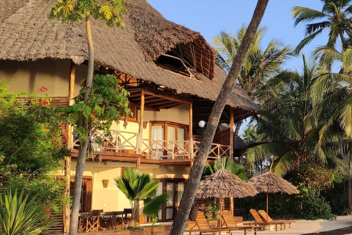 A resort with thatched-roof buildings, wooden balconies, and lounge chairs by a pool.
