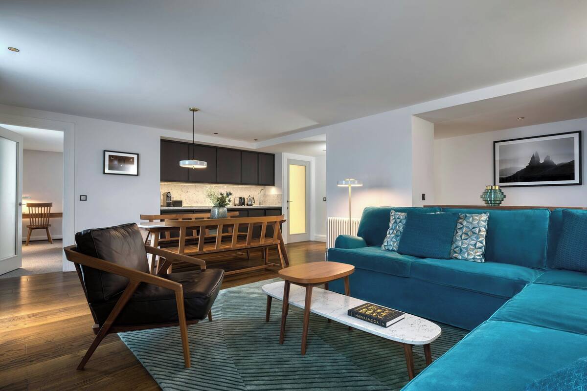 A modern living room with a blue sofa, a wooden coffee table, and a leather chair.