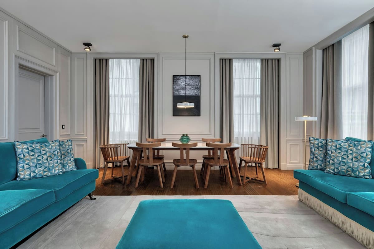 A modern living room with teal sofas, a dining table with chairs, and a chandelier.