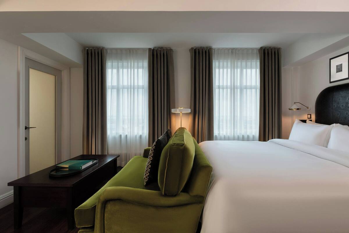 A hotel room with a large bed, a green sofa, a desk with a lamp, and curtains on the windows.