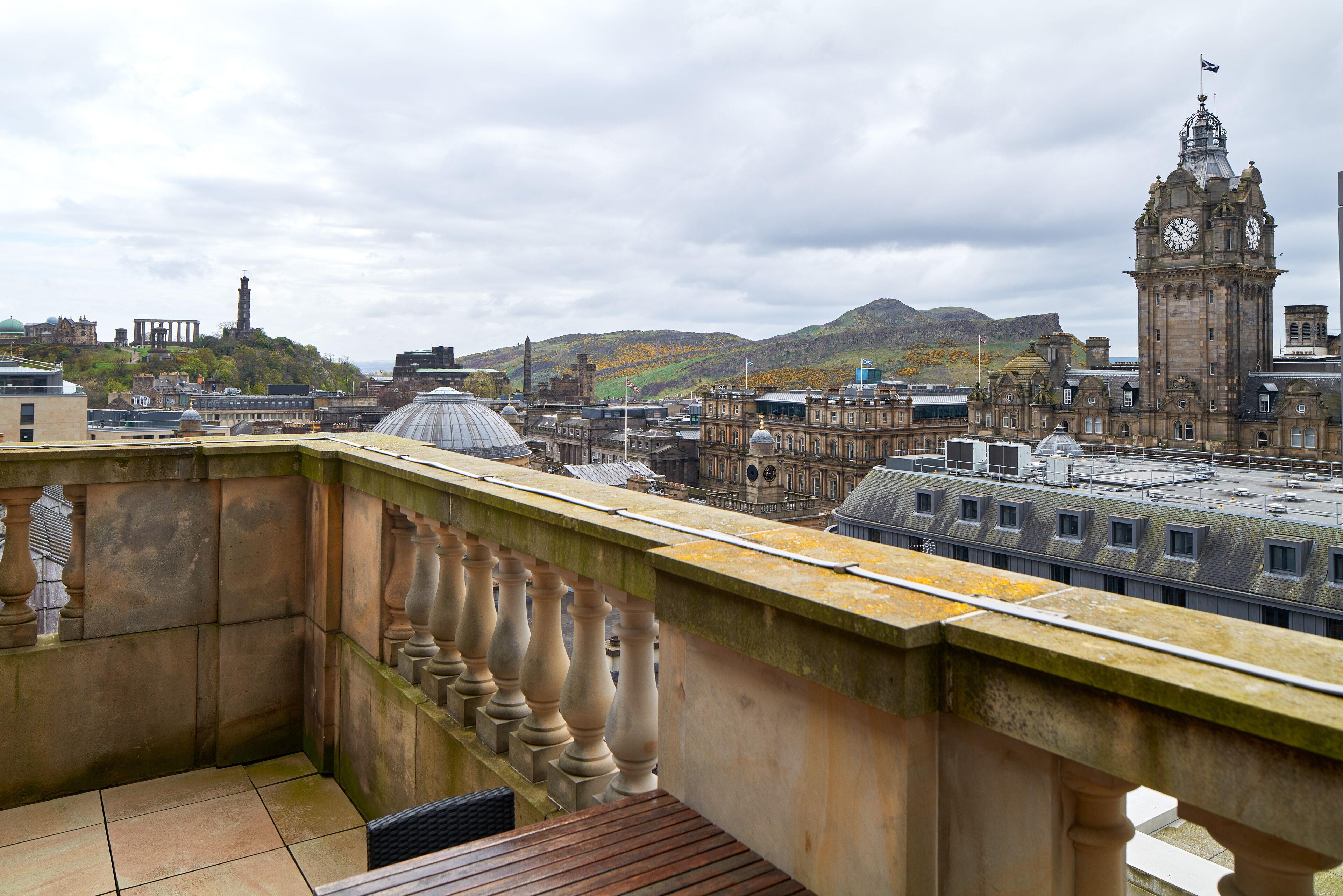 A balcony with a view of historic buildings, including a clock tower, and a mountain in the background.