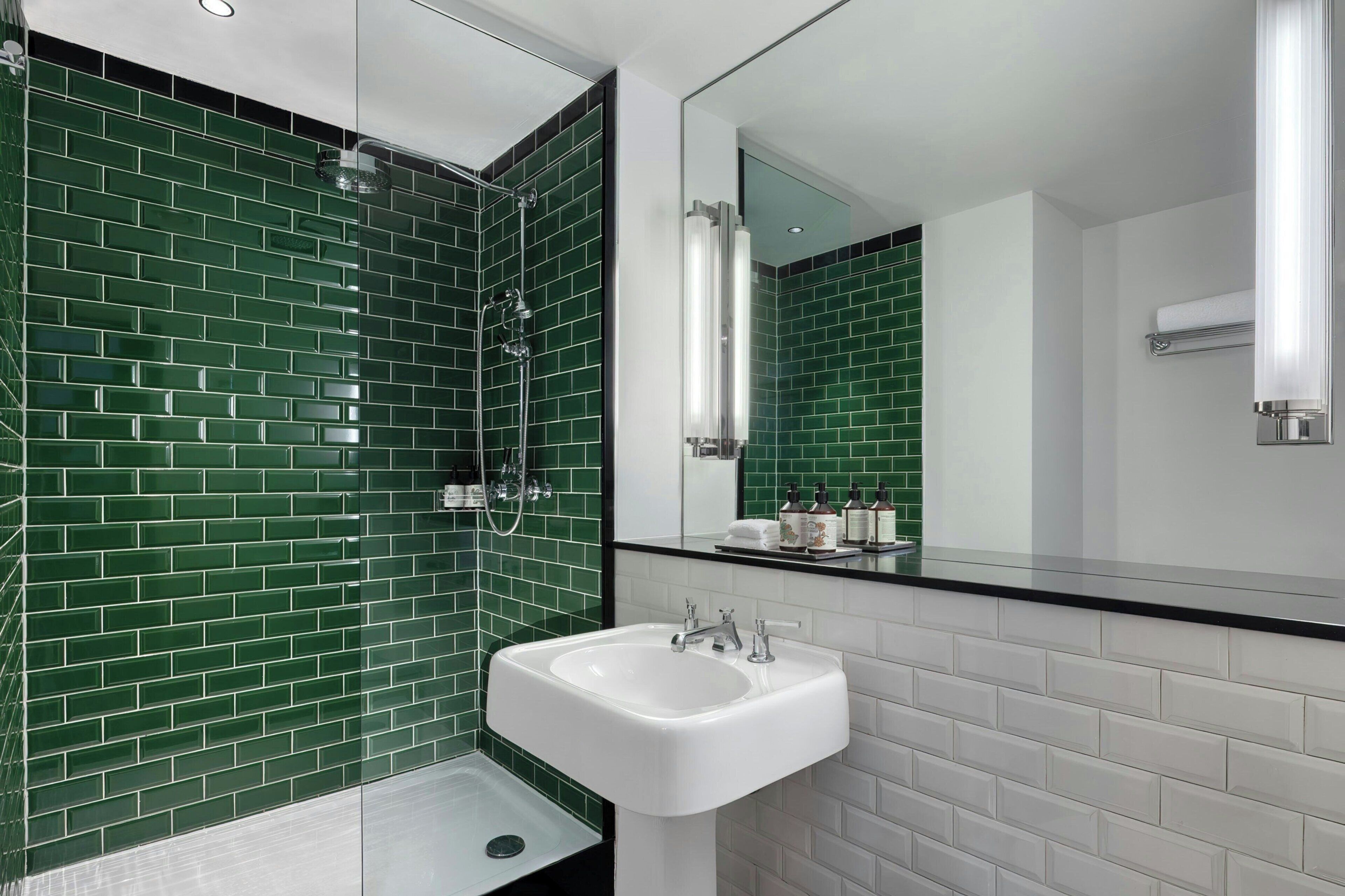 A modern bathroom with green-tiled walls, a white sink, and a large mirror.