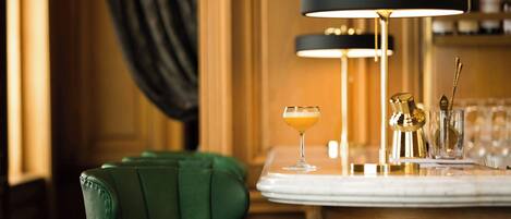 Uma área de bar com uma poltrona estofada em verde, uma mesa de mármore e um candeeiro de bar preto e dourado.