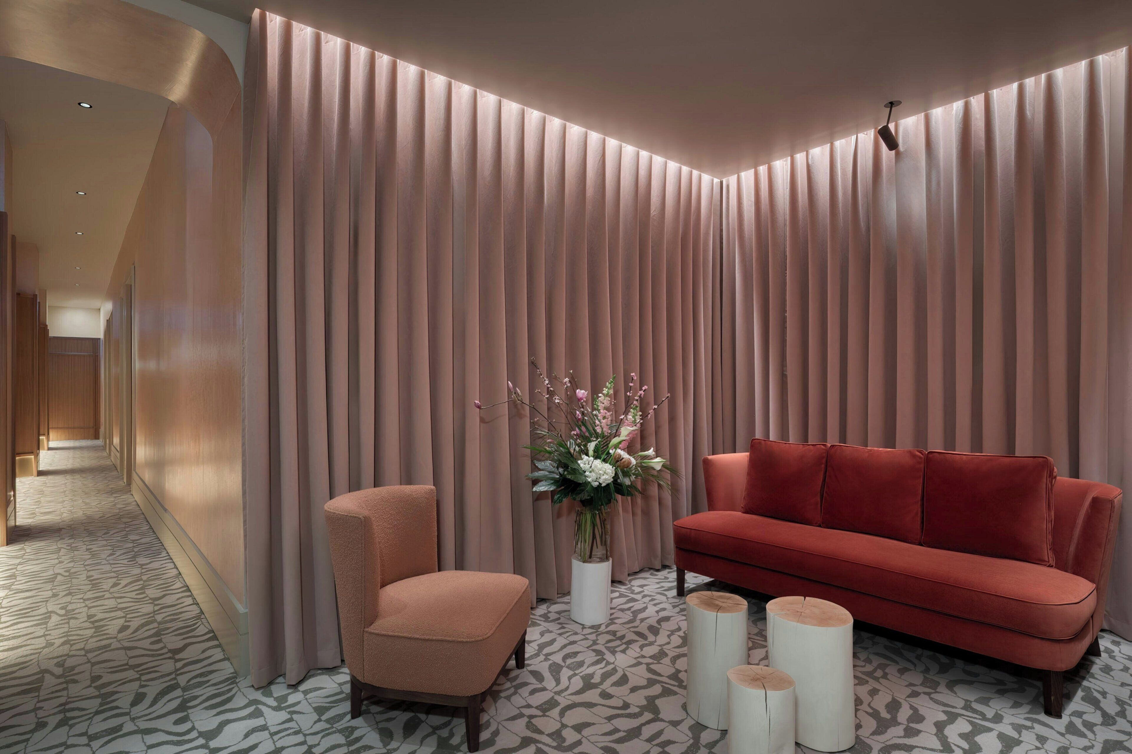 Un interior moderno con un sofá rojo, un sillón acolchado, un jarrón decorativo y un suelo estampado.