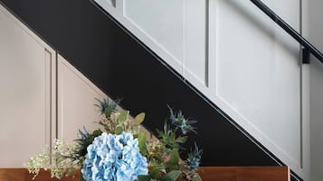 Un interior moderno con una lámpara negra, un jarrón con flores azules y una escalera.