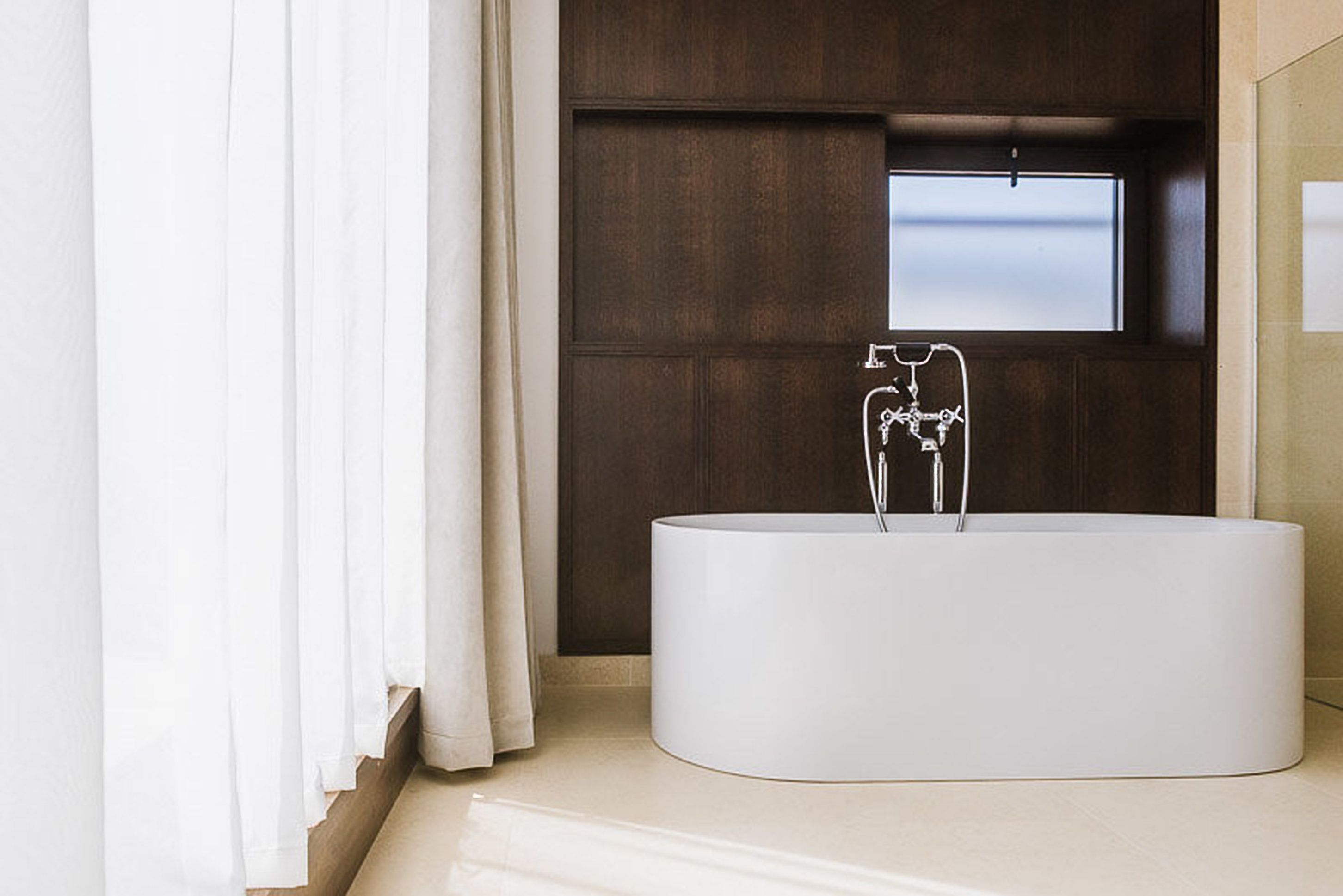 A modern bathroom with a freestanding bathtub, a window, and a wooden panel wall.