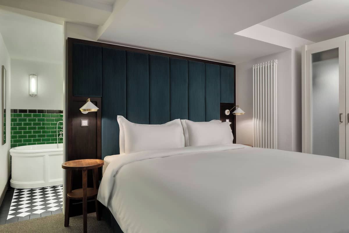 A hotel room with a large bed, a small table, a bathtub, and a green tiled wall.