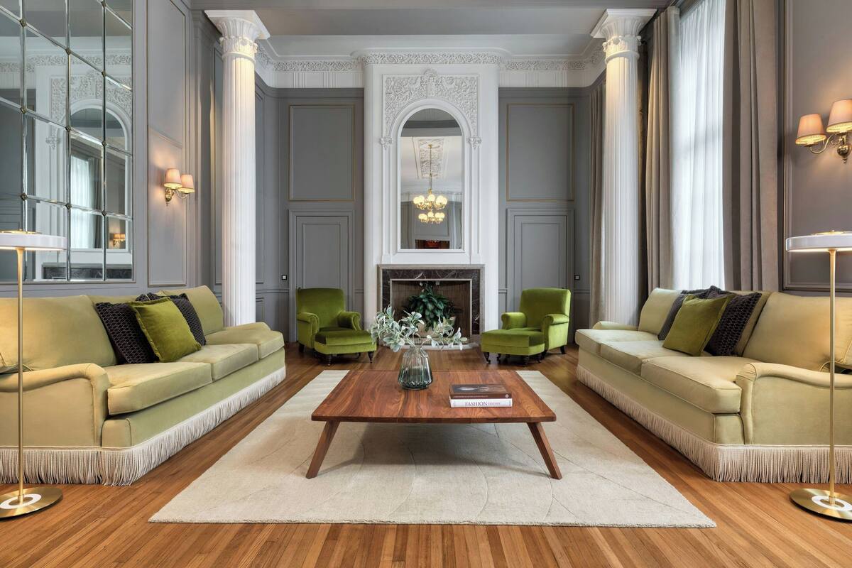 A spacious living room with a large wooden coffee table, two green armchairs, and a beige sofa.
