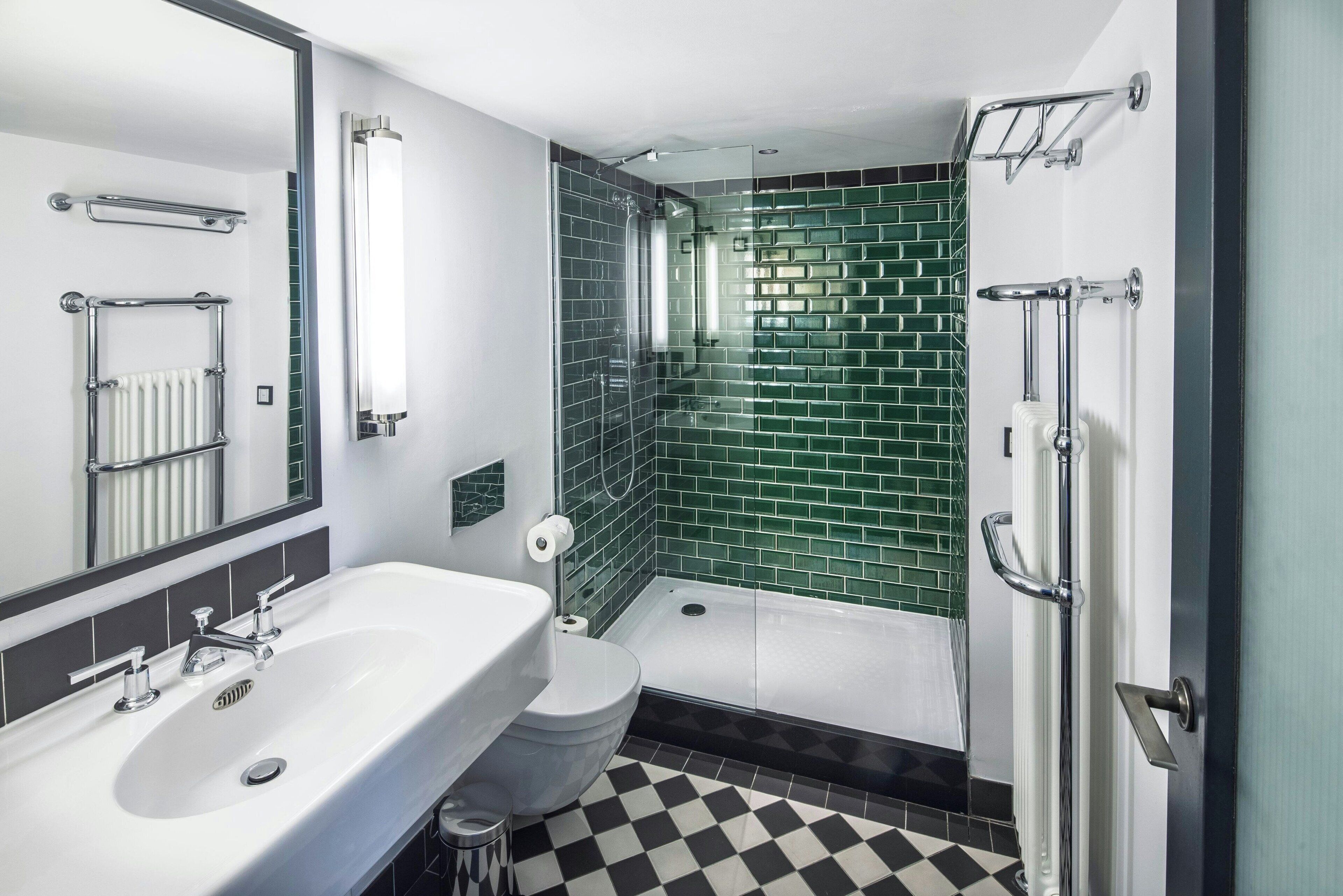 Un baño moderno con un lavabo blanco, un inodoro, una ducha con puerta de cristal y pared de ducha con azulejos verdes.